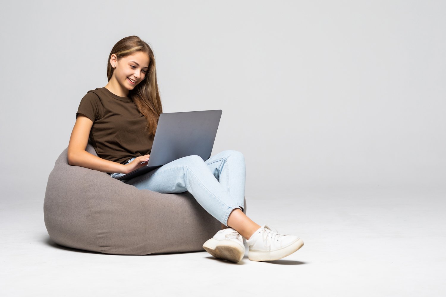 happy-young-woman-sitting-floor-using-laptop-gray-wall